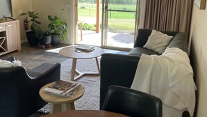 A living room with a sofa, a coffee table, and a TV. There is a sliding glass door leading to a garden. - Vista 2 drop the bags and look at the view (Yarra Junction)