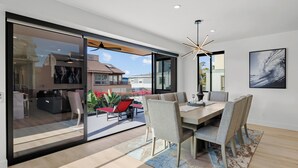 A modern dining area with a large table, chairs, and a view of the outdoors. - Brand New w/ Luxury Amenities | AC | Fire Pit | Walk to Beach, Bay, Shops, Eateries (San Diego)