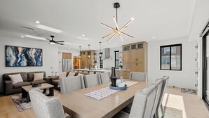 A modern kitchen with wooden cabinets, a central island, and pendant lighting. - Brand New w/ Luxury Amenities | AC | Fire Pit | Walk to Beach, Bay, Shops, Eateries (San Diego)
