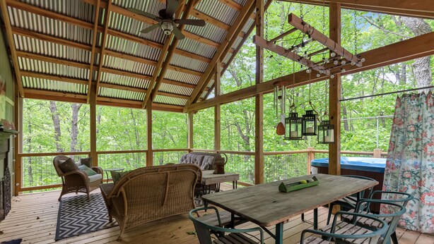Un espacio al aire libre techado con una mesa y sillas de madera, mobiliario de mimbre y faroles colgantes.