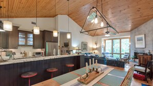 Una cocina moderna con techo de madera, taburetes de bar y un comedor con una mesa larga.