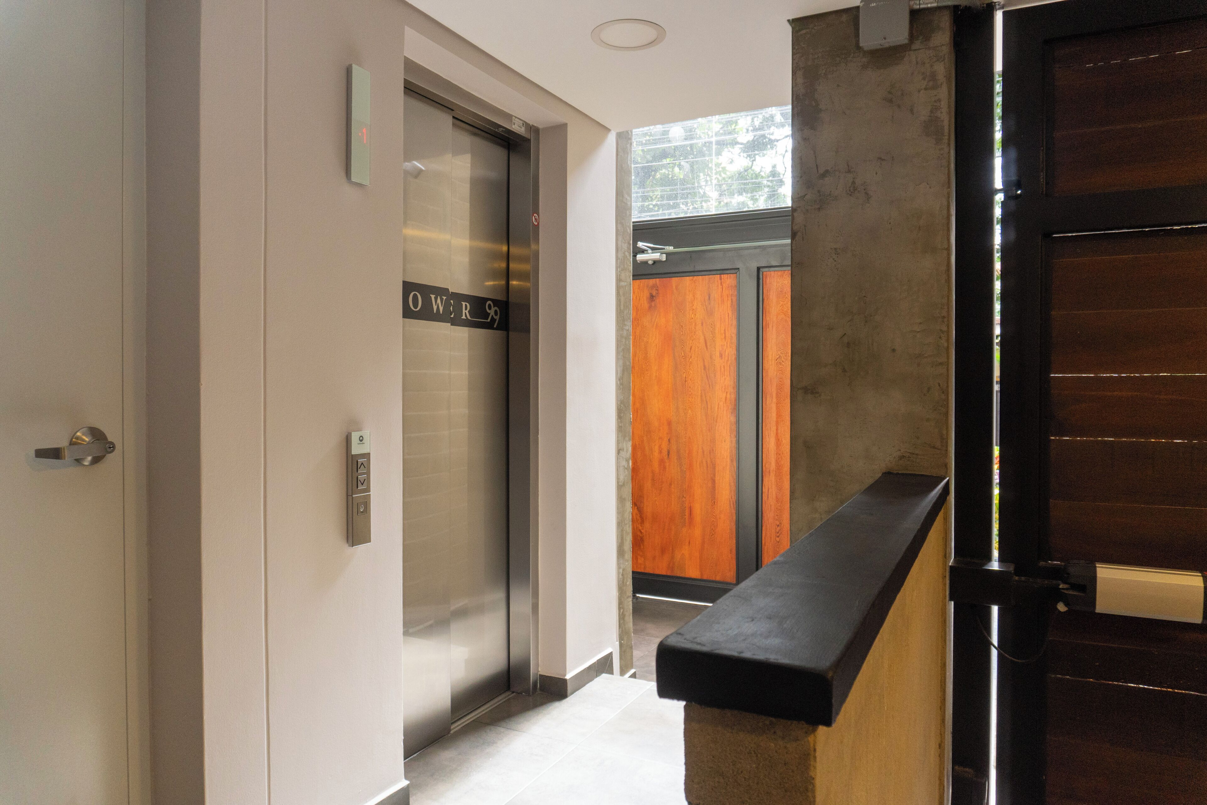 Un couloir avec un ascenseur portant l’inscription « OUIR 99 » et une porte en bois.