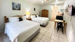Une chambre d’hôtel avec deux lits, un bureau, une chaise, un ventilateur de plafond et un téléviseur.