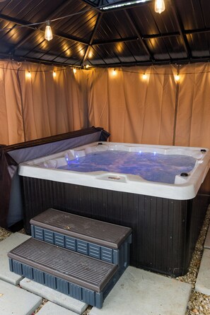 A hot tub with steps leading up to it, surrounded by a covered area with string lights.