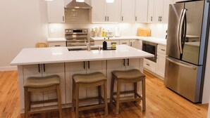 A modern kitchen with white cabinets, a stainless steel refrigerator, and wooden stools.