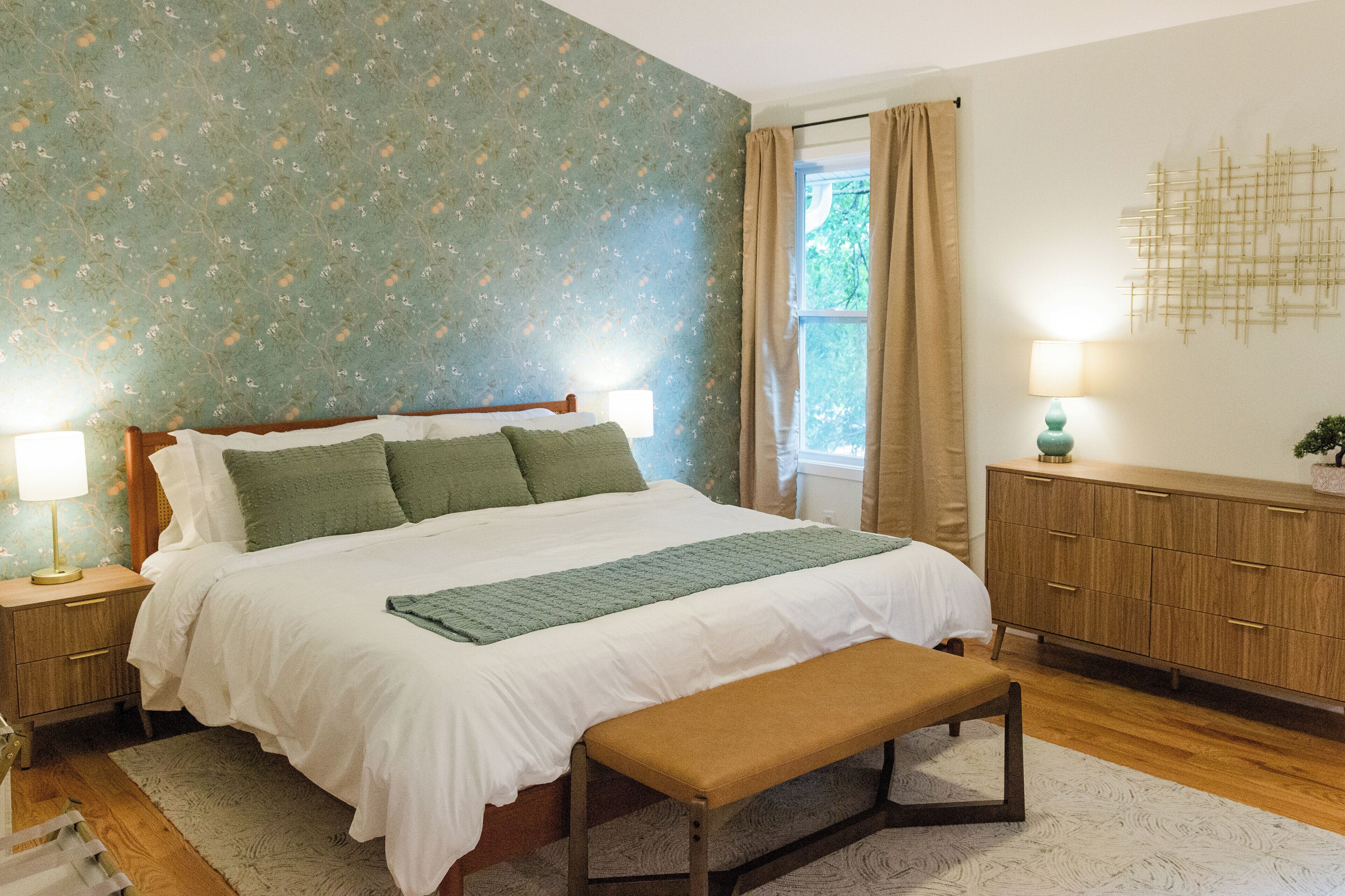 Une chambre à coucher bien rangée, avec un lit, un banc, des tables de chevet et une commode.