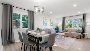 A modern living room with a dining area, large windows, and a view of greenery. - Upscale Old Town Views 3BD Lux (Alexandria)