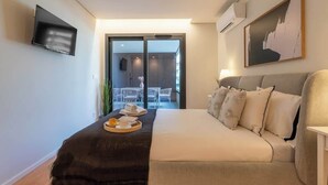 A modern bedroom with a bed, a flat-screen TV, a painting, and a view of the outside.