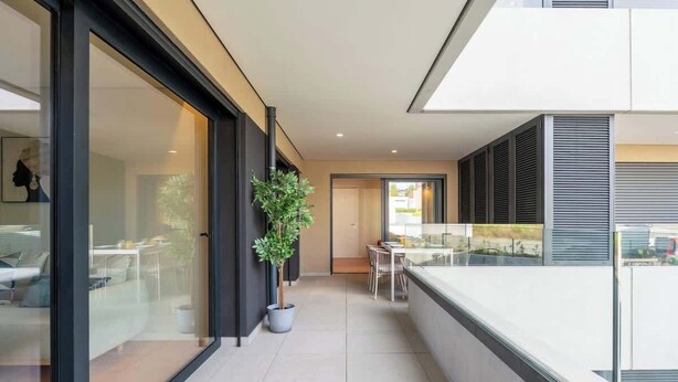 A modern interior with a glass door entrance, a potted plant, a dining area with a table and chairs, and a view of the outside.