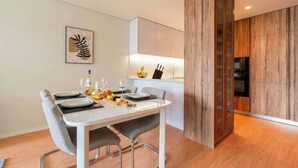 A modern dining area with a white table set for four, a wooden accent wall, and a kitchen area with wooden cabinets and a black refrigerator.