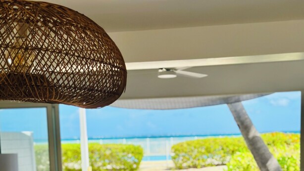 Un salón moderno con vista a la playa, una cesta de mimbre y un ventanal grande.