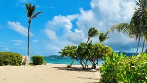 Dos tumbonas en una playa arenosa, con vista despejada al océano y palmeras al fondo.