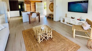 Un salón amplio con una gran televisión de pantalla plana, un ventilador de techo y un comedor con una mesa y sillas de mimbre.