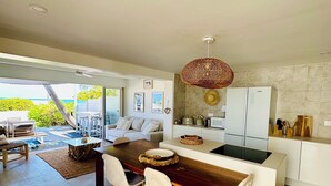 Una cocina moderna con una isla central, armarios blancos y vista al océano.