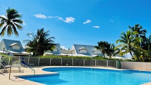 A swimming pool with lounge chairs and palm trees, surrounded by buildings with modern architecture. - Salty Beach - NBBC- 1 bedroom beachfront (Marigot)