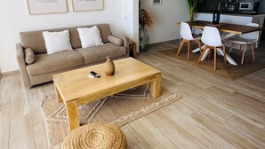 A modern living room with a sofa, coffee table, and chairs. There is a kitchen area in the background. - Salty Beach - NBBC- 1 bedroom beachfront (Marigot)