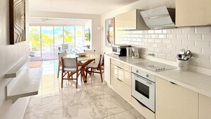 A modern kitchen with white cabinetry, a marble floor, and a dining area with a table and chairs. - Sea Breeze - NBBC - 2 bedrooms beachfront (Marigot)