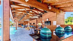 A covered outdoor area with a pool, wooden seating, and barbecue grills.