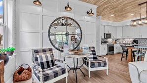 A modern kitchen with white cabinetry, a round mirror, and a dining area with checkered chairs.