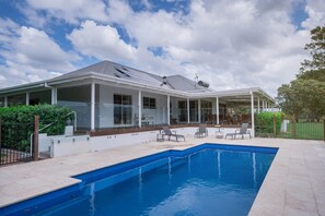 Una casa moderna con piscina, patio cubierto y jardín cercado.