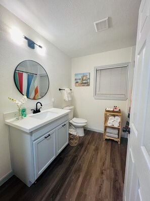 Un bagno con un mobile lavabo bianco, uno specchio rotondo, un water e un piccolo ripiano con asciugamani.