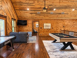 A room with a pool table, a sofa, a television, and a ceiling fan.
