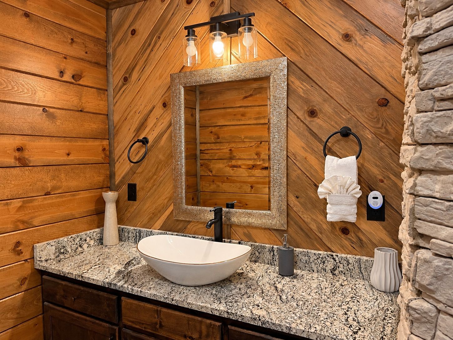 A bathroom with a wooden wall, a large mirror, a vessel sink, a towel ring, and a towel.