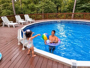 A swimming pool with a wooden deck, lounge chairs, and a safety fence.