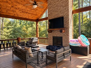 A covered outdoor area with a stone fireplace, seating, and a flat-screen TV.