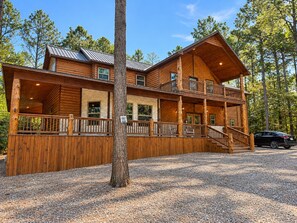 A two-story log cabin with a balcony, a covered porch, and a gravel driveway.