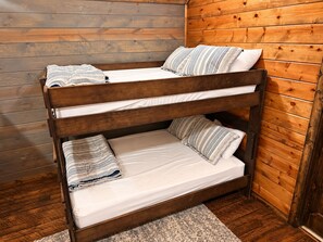 A bunk bed with white bedding and patterned pillows in a room with wooden walls.