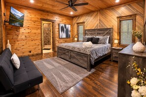 A bedroom with a large bed, a sofa, a TV, and a fireplace.