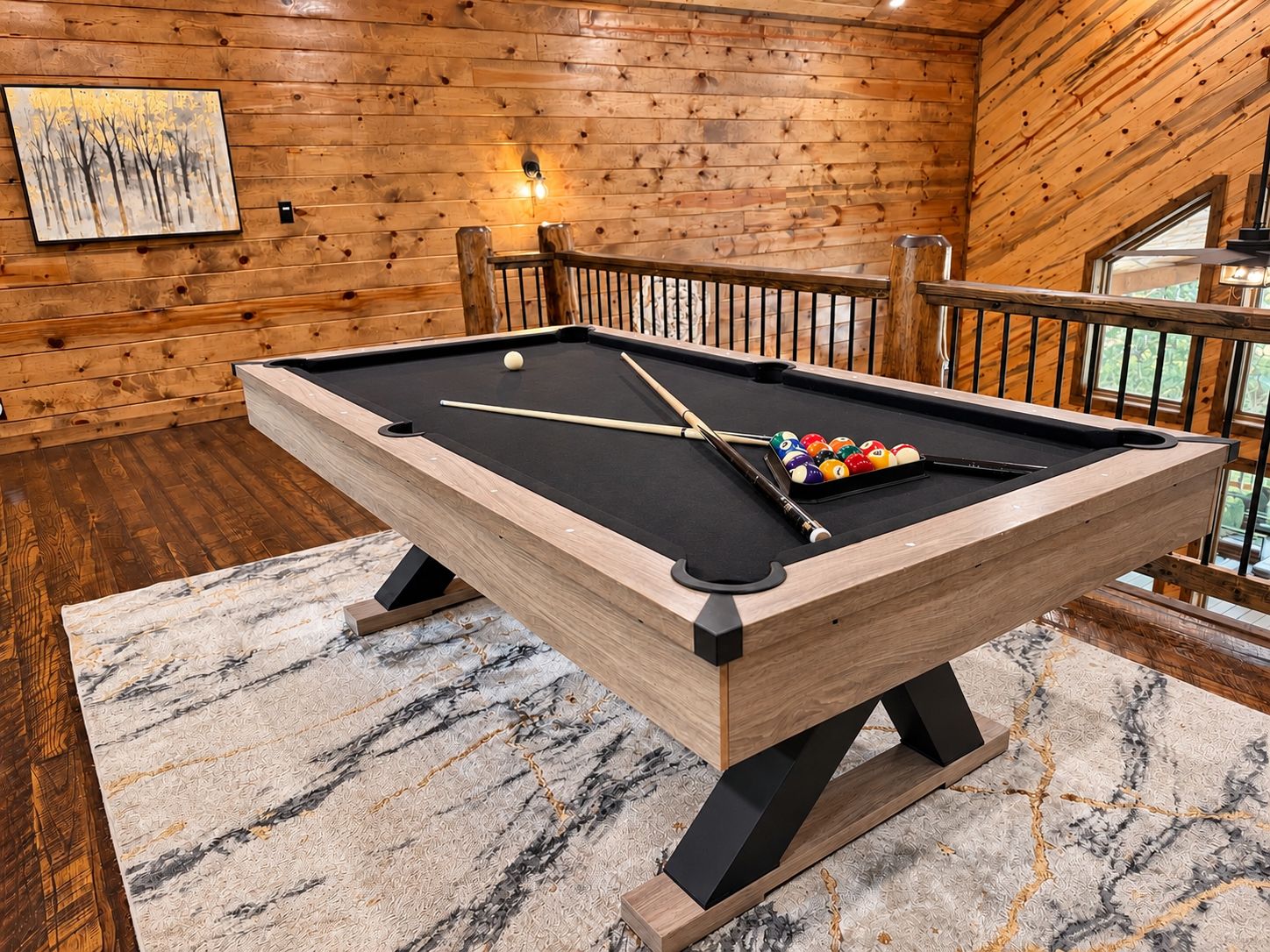 A pool table in a wooden room with a railing and a painting on the wall.