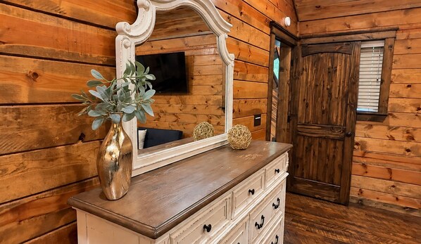 A wooden interior with a dresser, a mirror, a plant, and a door.