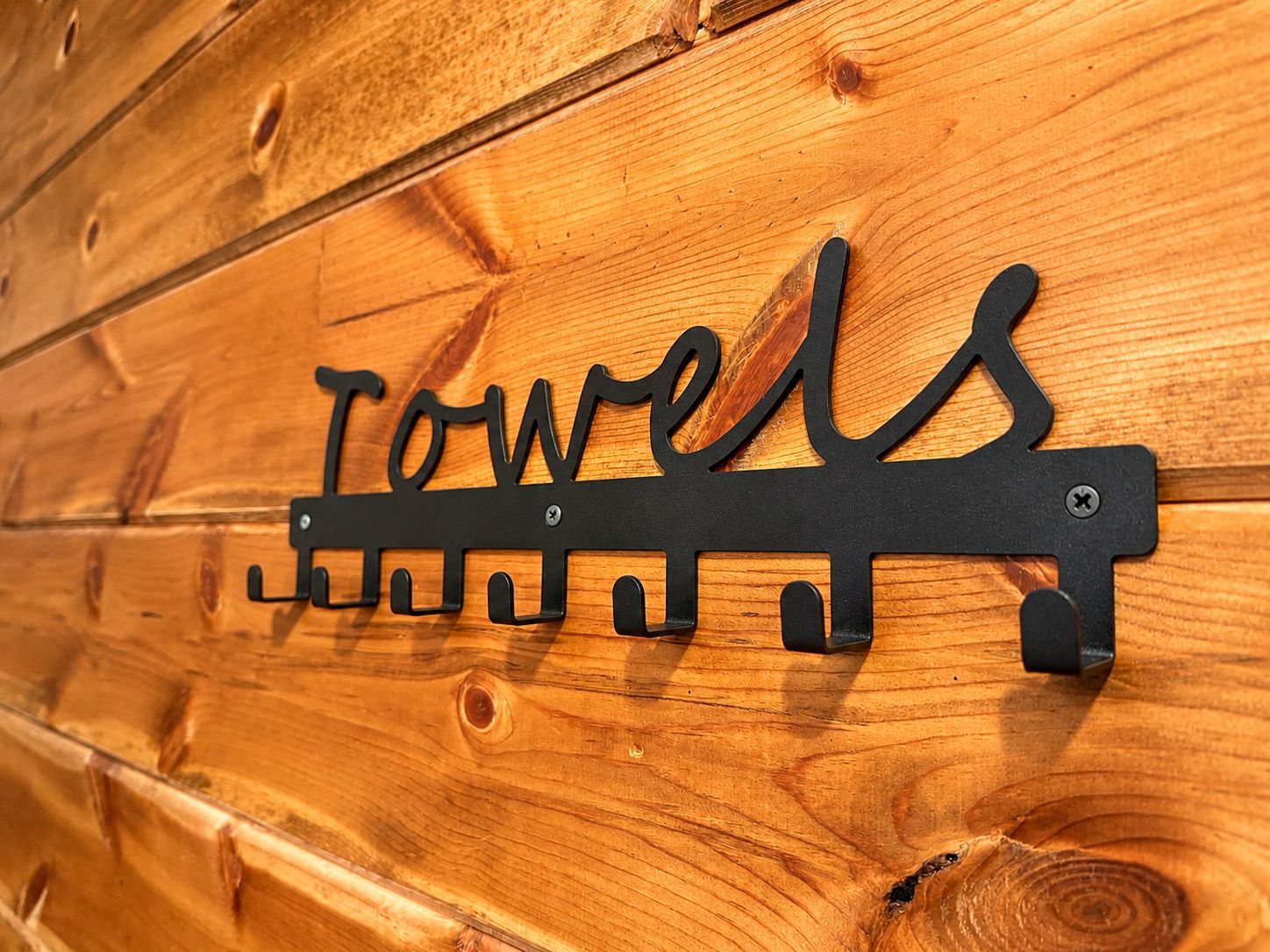 A black metal sign with the word 'TOWELS' mounted on a wooden wall.
