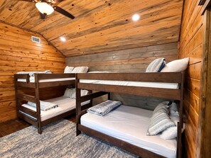 Una cabaña con paredes de madera y techo inclinado. Hay literas con almohadas y mantas.