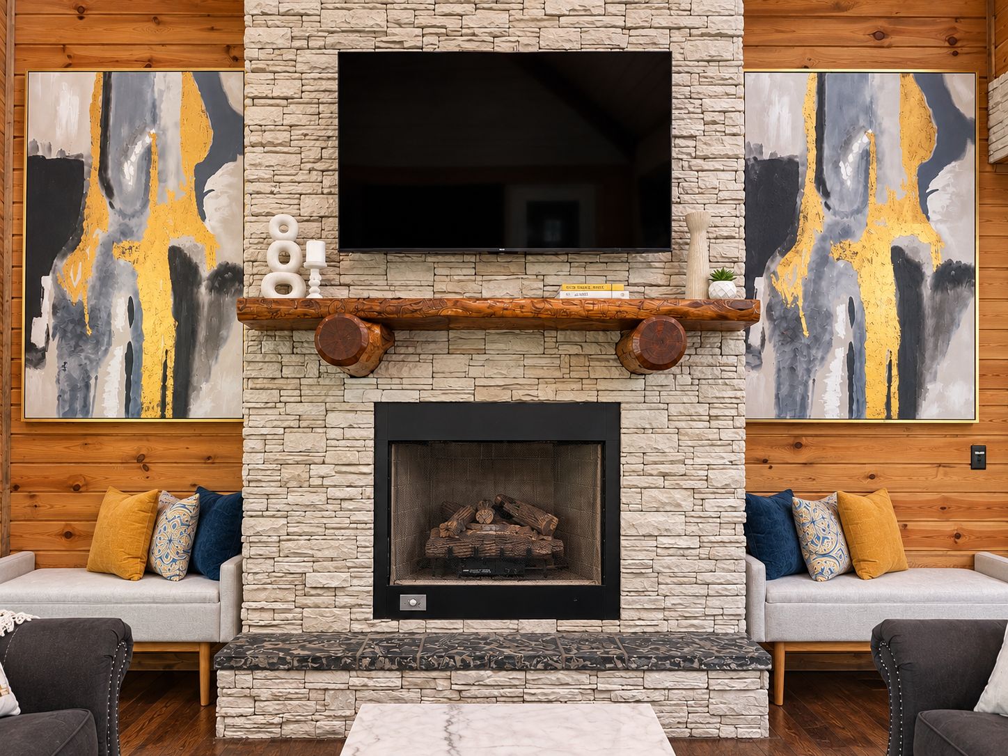 Una sala de estar con chimenea de piedra, un televisor de pantalla plana montado y arte abstracto en las paredes.