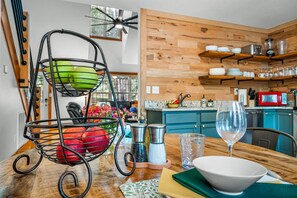 Una cocina con armarios de madera, una mesa de comedor con un tazón y una copa de vino, y una cesta de fruta.