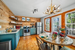 Una cocina con paredes de madera, una mesa de comedor con sillas, una araña y vistas amplias a través de grandes ventanales.