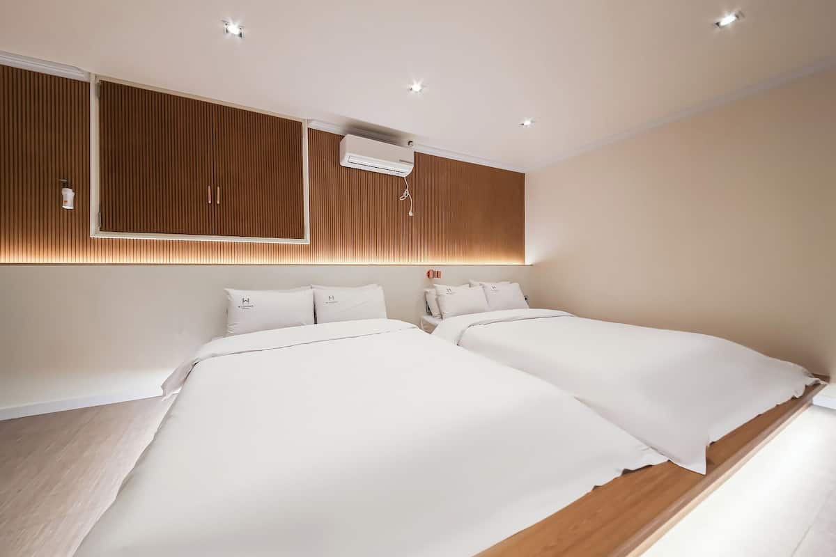 Une chambre d’hôtel moderne avec deux lits, une tête de lit en bois, des spots encastrés au plafond et un appareil de climatisation.