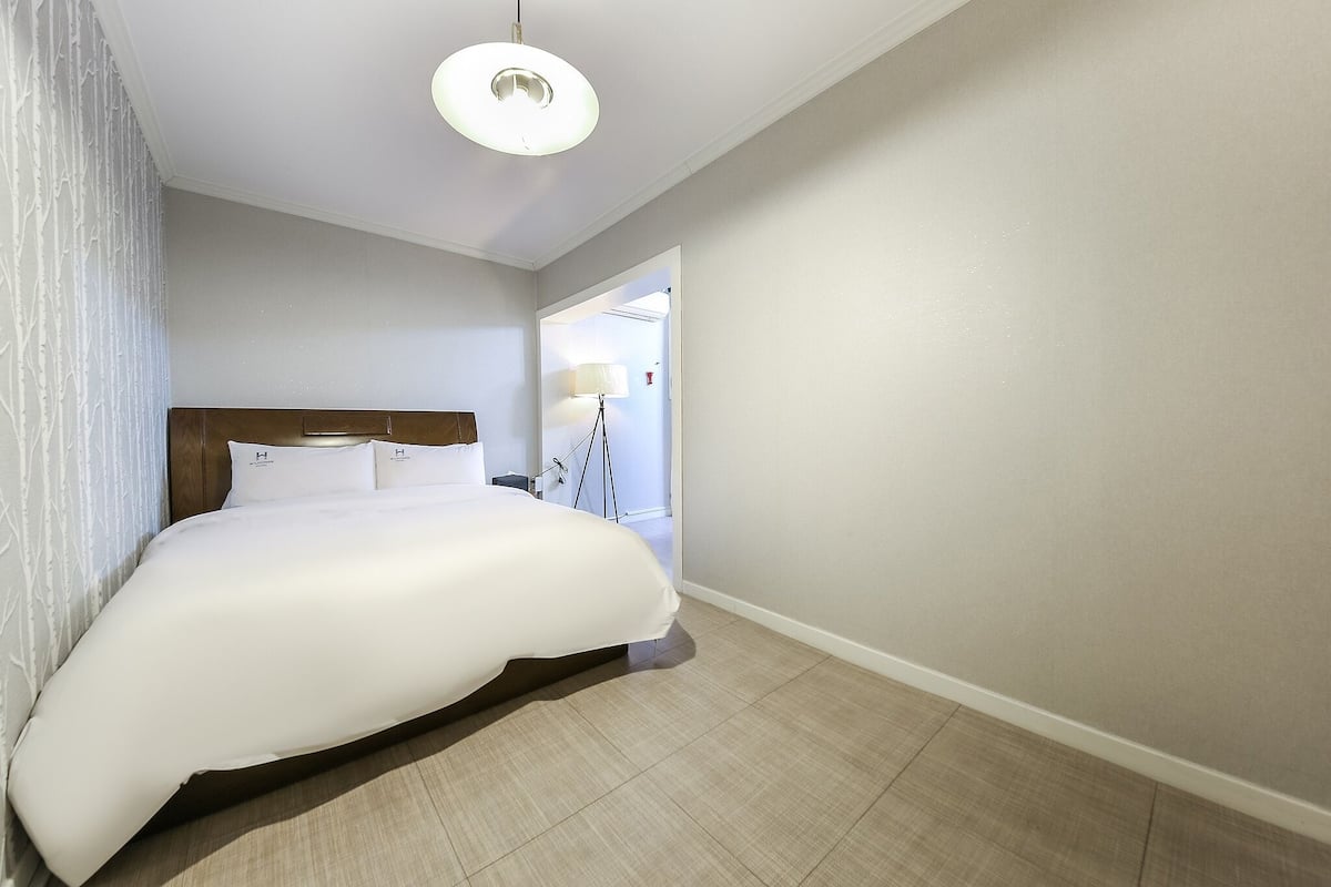 Une chambre d’hôtel avec un grand lit, une tête de lit en bois, un luminaire au plafond et une vue sur le couloir.
