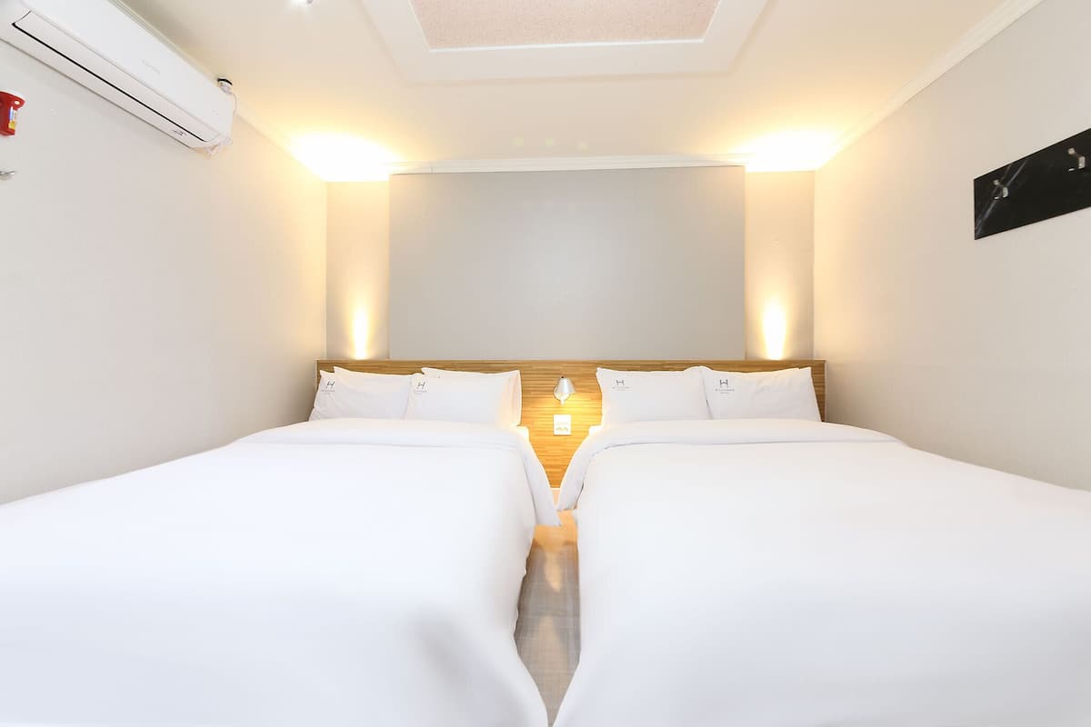 Une chambre d’hôtel avec deux lits simples, une tête de lit en bois, un climatiseur fixé au mur et un luminaire au plafond.