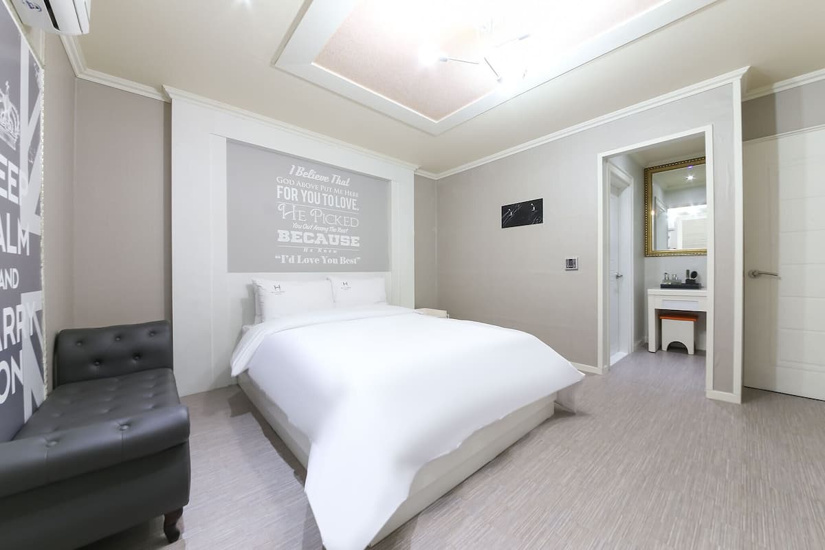 Une chambre moderne avec un grand lit, un petit canapé, un mur orné de citations inspirantes, un petit bureau et un miroir.