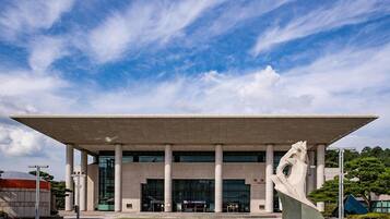 A modern building with a flat roof, large columns, and a central sculpture.