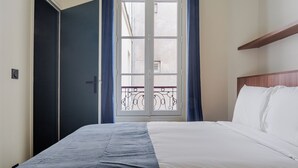 Une chambre d’hôtel avec un lit, une armoire, une fenêtre avec des rideaux et un balcon donnant sur une vue agréable.