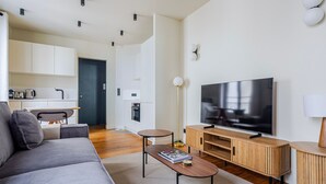 Un salon moderne avec un canapé, une table basse, un téléviseur et, au fond, un coin cuisine.