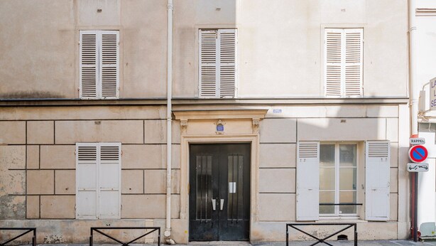 Un bâtiment avec une porte noire, des volets blancs et un panneau indiquant qu’il est interdit de se garer.