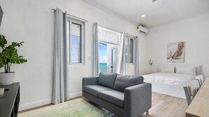 A modern bedroom with a grey sofa, a bed, and a view of the sea through the windows. - Ocean Pearl Estate (Nassau)