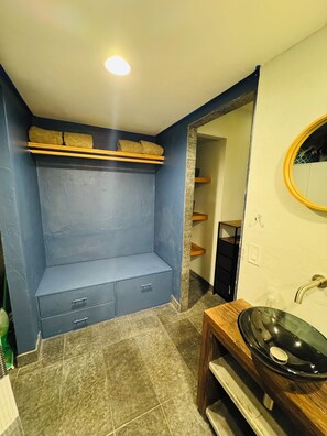 Un bagno con un mobiletti blu, uno scaffale in legno, uno specchio rotondo e un lavandino nero.