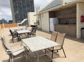Una terrazza esterna con tavolo e sedie, un'area barbecue e vista su un edificio alto sullo sfondo.